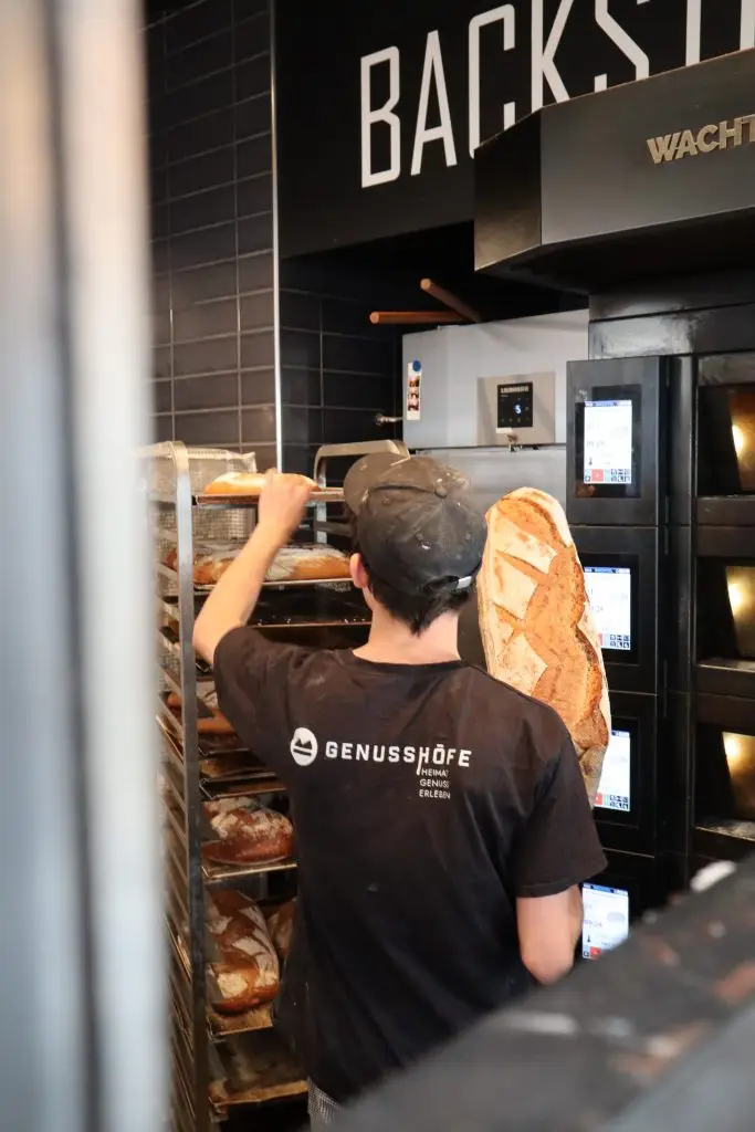 Ein Mann mit einem Genusshöfe-Shirt steht in einer Backstube und sortiert Brot ein