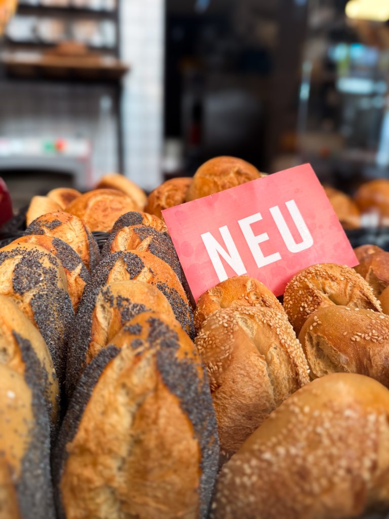 Mohn- und Sesambrötchen in einem Korb aufgereiht mit einem roten Schild mit der Aufschrift "Neu"