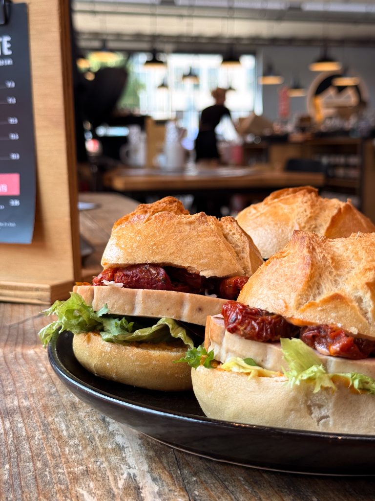 3 Belegte Brötchen mit Leberkäse, Salat und getrockneten Tomaten auf einem Teller in einem Kaffeehaus.